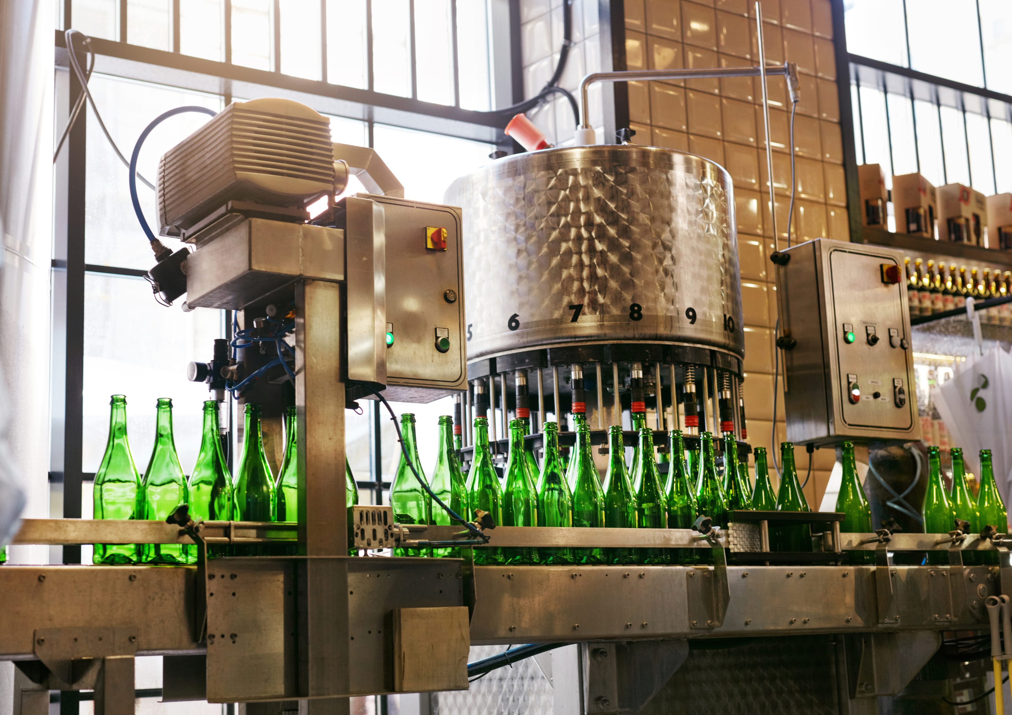 Automated glass bottling line in a brewery, showing green bottles being filled and capped by industrial machinery.